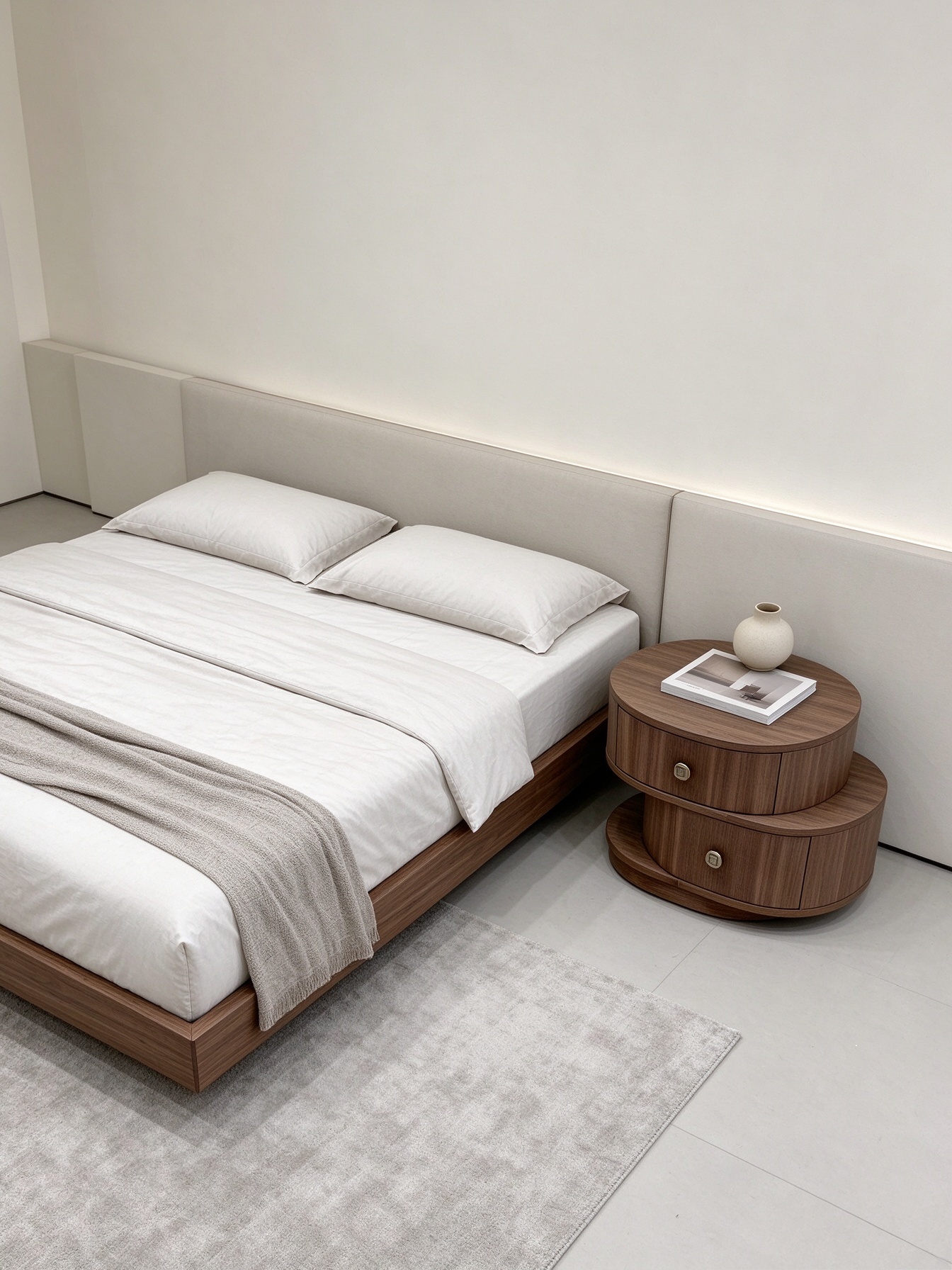 Asymmetrical round walnut nightstand styled beside upholstered bed, warm walnut finish