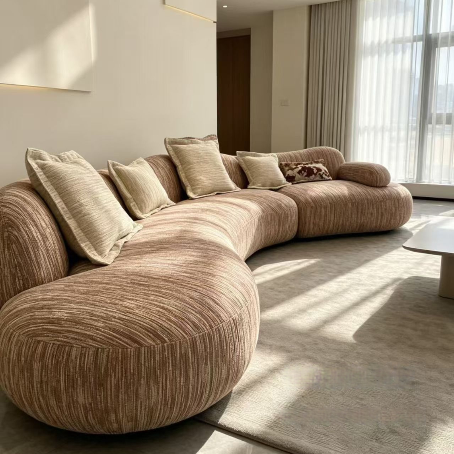 Cream beige curved bouclé-style sofa in a wabi-sabi living room with a travertine coffee table, large windows, and mountain views
