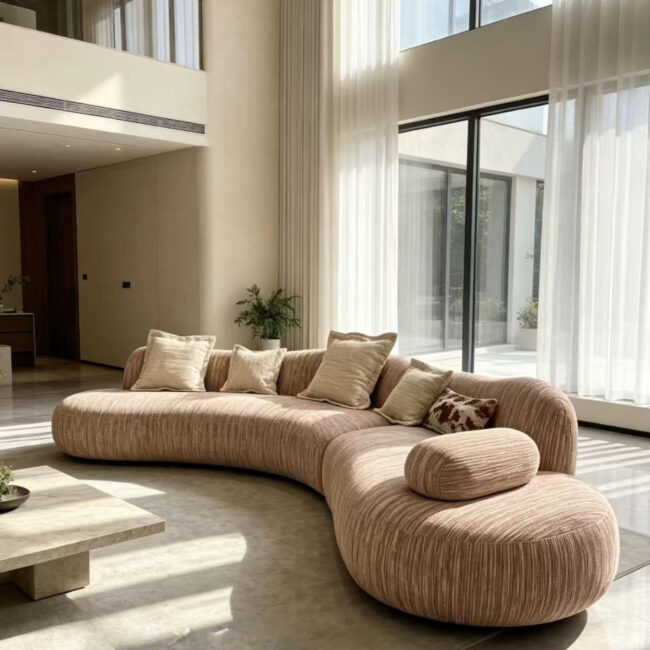 Taupe ribbed curved modular sofa in a modern wabi-sabi living room, paired with a beige rug and a round travertine coffee table.