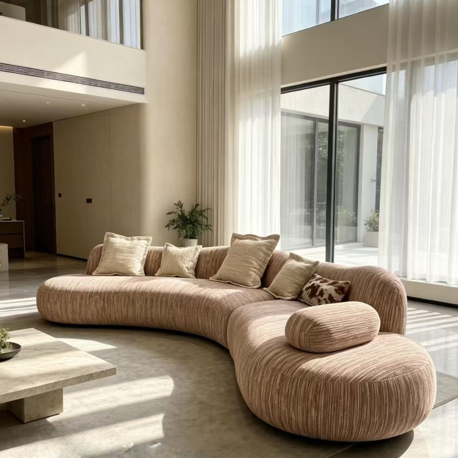 Taupe ribbed curved modular sofa in a modern wabi-sabi living room, paired with a beige rug and a round travertine coffee table.